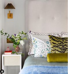 a bed with blue and green pillows on top of it next to a white night stand