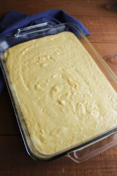 a casserole dish with yellow batter in it on a wooden table next to a blue cloth