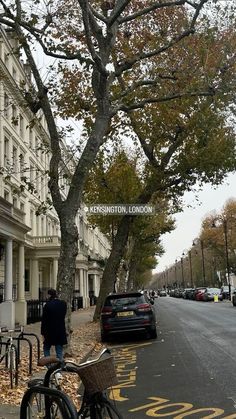 a bicycle parked on the side of a street next to a tree and buildings with cars