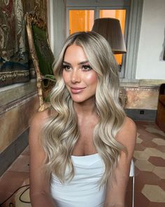 a woman with long blonde hair is sitting in a room and smiling at the camera