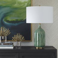 a green vase sitting on top of a wooden table next to a lamp and books