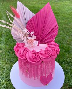 a pink cake with an umbrella and feathers on top is sitting in the green grass