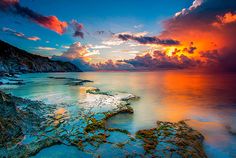 the sun is setting over an ocean with rocks and algae growing on it's shore