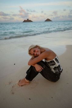 a woman sitting on top of a sandy beach next to the ocean with her arms crossed