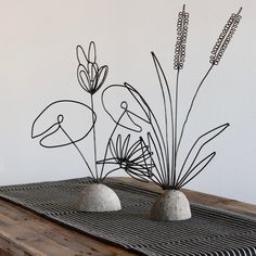 two metal sculptures sitting on top of a wooden table next to each other and plants in the middle