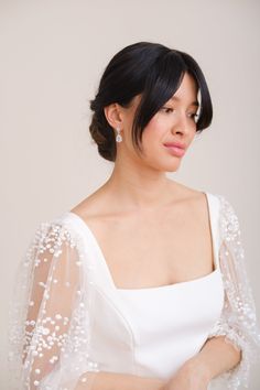 a woman wearing a white wedding dress with sheer sleeves and beading on her shoulders