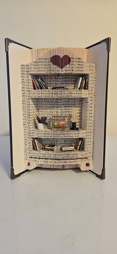 an open book with bookshelves made out of old newspaper strips and paper hearts