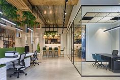 an office with glass walls and plants hanging from the ceiling, along with chairs and desks