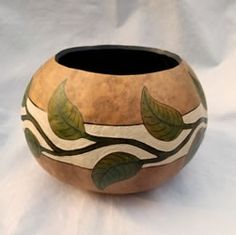 a vase with leaves painted on it sitting on a white cloth covered tablecloths