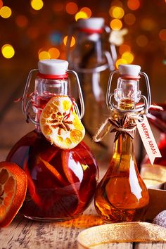 two bottles filled with liquid sitting on top of a wooden table next to sliced oranges