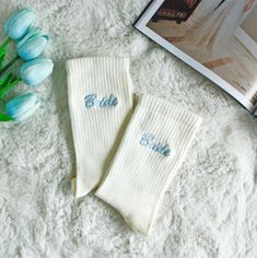 two white socks with blue lettering on them next to tulips and a book