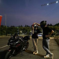 two people standing next to a motorcycle in a parking lot with a crane behind them