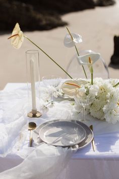 a table set with white flowers and candles on the beach for an elegant wedding reception