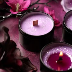 three candles are sitting next to each other on a table with pink flowers and purple petals