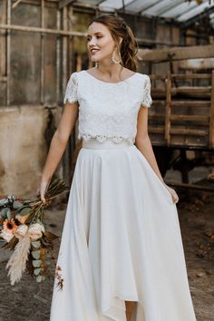 a woman wearing a white dress and holding a flower bouquet in her hand while standing outside