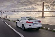 a white car driving down the road next to a large suspension bridge with a sunset in the background