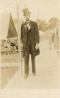 an old black and white photo of a man in a suit with a cane standing on a boardwalk