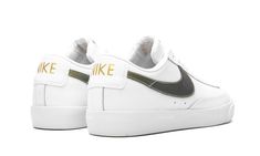 The Nike Blazer Low Premium is one of the brand's most iconic sneakers, and here we see it reinvigorated again in a crisp “White/Metallic Gold” colorway.  In understated fashion, the low top Nike shoe features a smooth white leather upper with tonal stitching and an all-white lacing system.  Giving contrast to the sleek look is an olive green Nike Swoosh on the side with metallic gold stitching.  The same gold accent color also appears on the Swoosh labeling the tongue and "NIKE" branding on the Understated Fashion, Low Top Nikes, Olive Green Nike, Metallic Gold Shoes, Iconic Sneakers, Nike Blazer Low, Nike Branding, Nike Shoe, Blazer Low