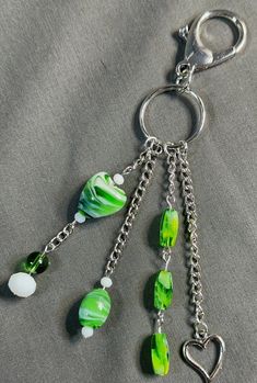 a green and white beaded keychain hanging from a metal hook on a gray cloth