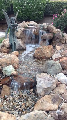 a garden with rocks and water features a statue of an angel holding a staff over a waterfall