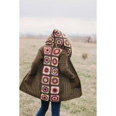 a woman is walking in the grass wearing a brown coat with crocheted flowers on it