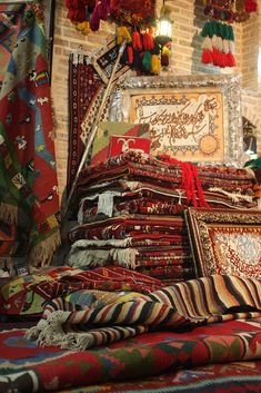 an assortment of rugs and scarves on display in a room with brick walls