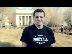 a man standing in front of a white building with trees and bushes behind him, wearing a football t - shirt