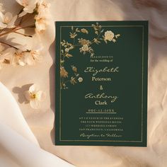 a wedding card with flowers on it next to a white flowery bouquet and ribbon