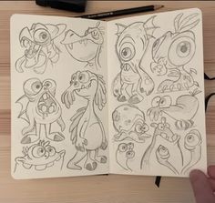 an open notebook with drawings of cartoon characters on the pages, and a hand holding a pen