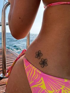 a woman with a flower tattoo on her lower back, standing next to the water