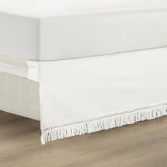 a white bed skirt with fringes on the bottom and side rails, in front of a wooden floor