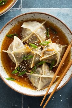 two bowls filled with dumplings and chopsticks on top of a blue table