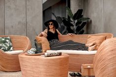 a woman sitting on a wicker couch next to two chairs and a coffee table