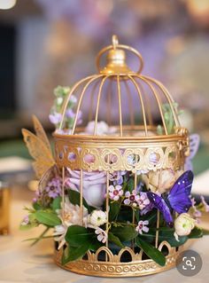 a birdcage filled with flowers and butterflies on top of a table