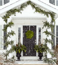 a white house covered in snow with evergreens and wreath on it's front door