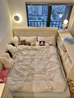 there are stuffed animals on the bed in this small room with a window overlooking the city