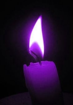 a lit candle in the dark with purple light