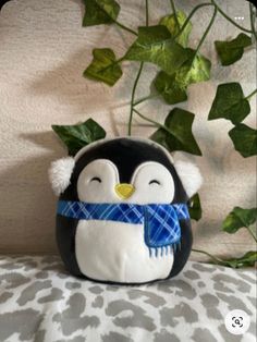 a stuffed penguin with a scarf around its neck sitting on a bed next to ivy