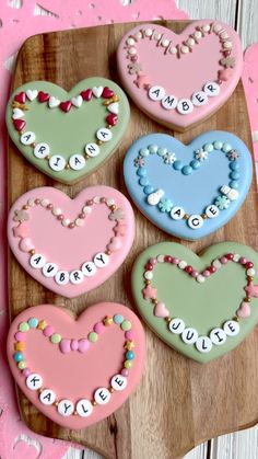 four decorated heart shaped cookies sitting on top of a wooden cutting board