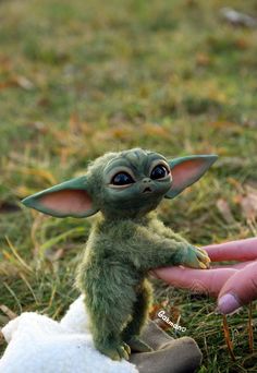 a tiny baby yoda doll being held by someone's hand in the grass