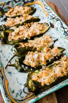 stuffed green peppers with cheese on top in a blue and yellow dish sitting on a wooden table