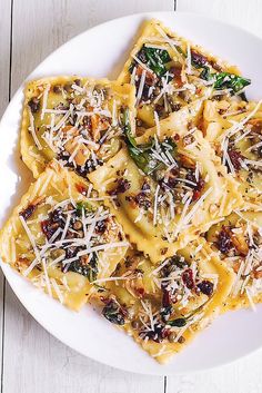 a white plate topped with ravioli covered in cheese and spinach sauce on top of a wooden table