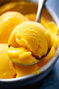 two scoops of yellow ice cream in a bowl with a spoon on the side