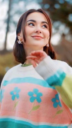 a woman in a colorful sweater is smiling and holding her hand out to the side