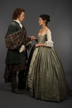 a man standing next to a woman in a dress on a gray background with a tartan