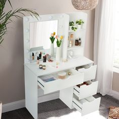 a white vanity table with drawers and lights on the top, next to a potted plant