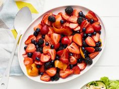 a white plate topped with fruit salad next to a bowl filled with berries and oranges