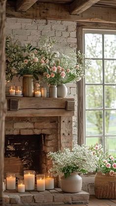 a fireplace with flowers and candles in front of the fire place, next to an open window