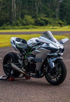 a silver motorcycle parked on top of a parking lot next to a lush green field