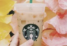 a person holding up a starbucks drink in front of flowers